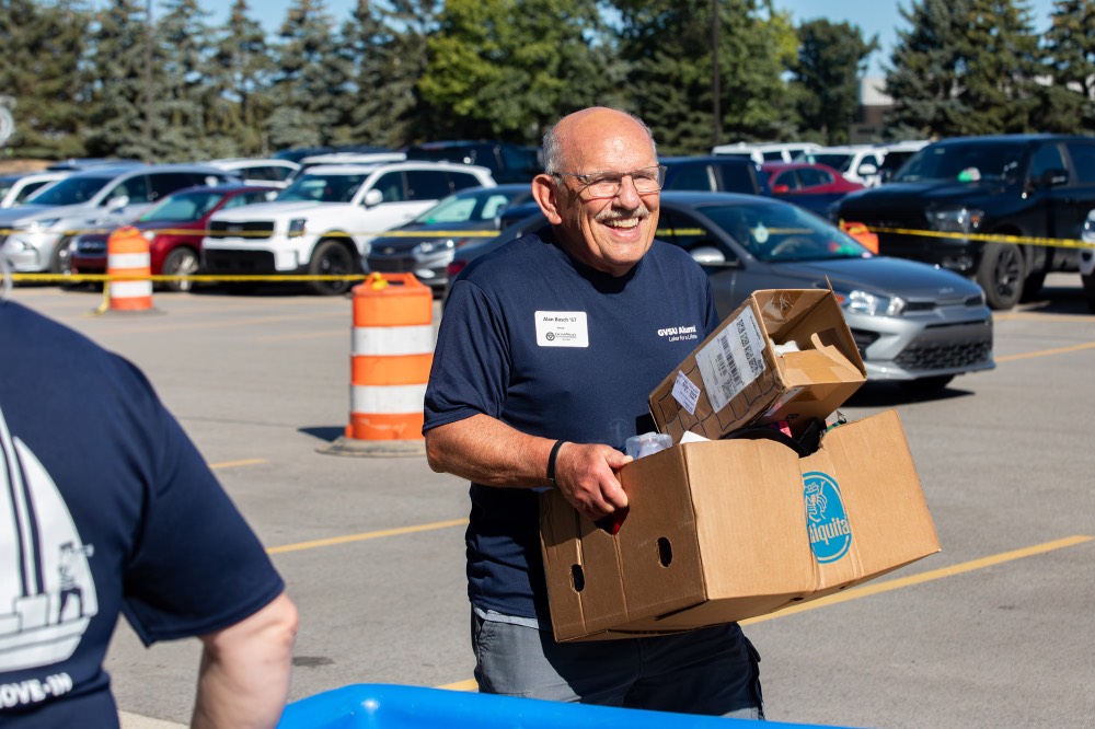 Class of 1967 Alumnus smiles as he carries in 2 cardboard boxes for new lakers